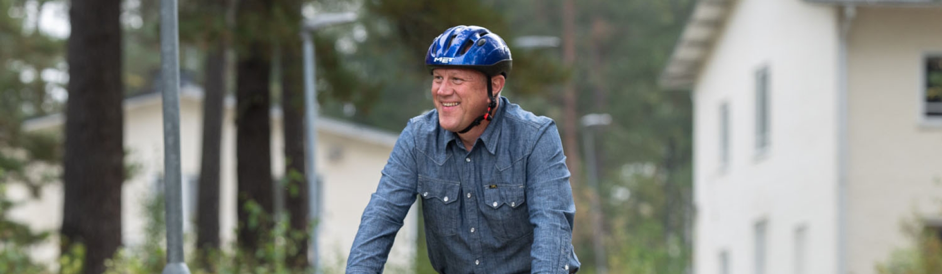En man i blå skjorta och cykelhjälm cyklar på en cykelväg